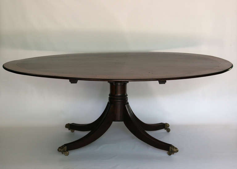 English Regency Mahogany and crossbanded  oval breakfast table.  Reeded Sabre support with brass cabs and casters.  Beautiful proportioned table.