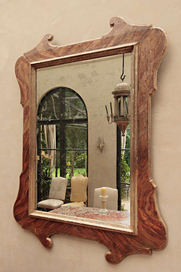A very large scale Tuscan mirror frame painted in faux marble with later glass added. This 19th Century mirror is from the region of Lucca in Northern Italy.  The faux painting is in shades of terracotta and brown.  The scroll detail on the top and