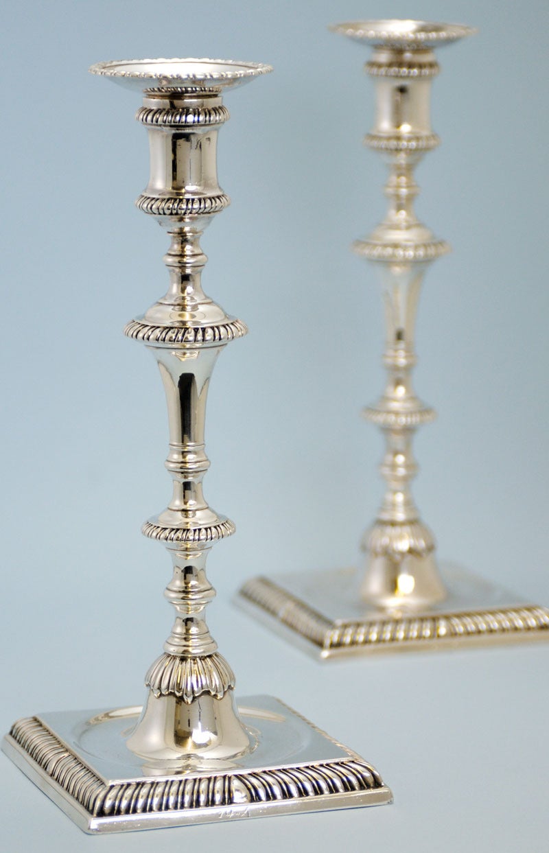 Extremely elegant pair of George III, sterling silver, cast candlesticks with a sunk centre to each base and detachable nozzels. Made in London in 1764 by Ebenezer Coker. Both square bases are engraved with a monogram of two slanting capital as