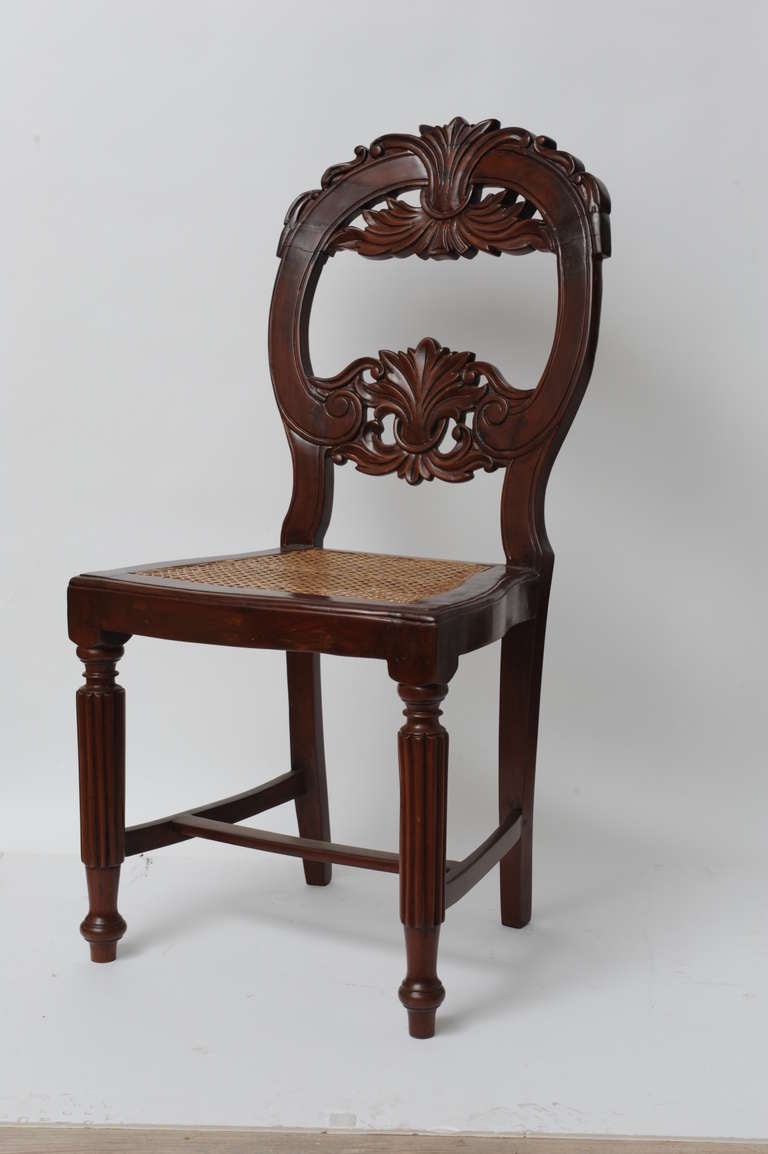Set of four rare rosewood dining chairs from Portuguese Goa, late 1800s. Caned seats have been redone. Beautifully carved crests and backs with reeded legs.  Cushions included.