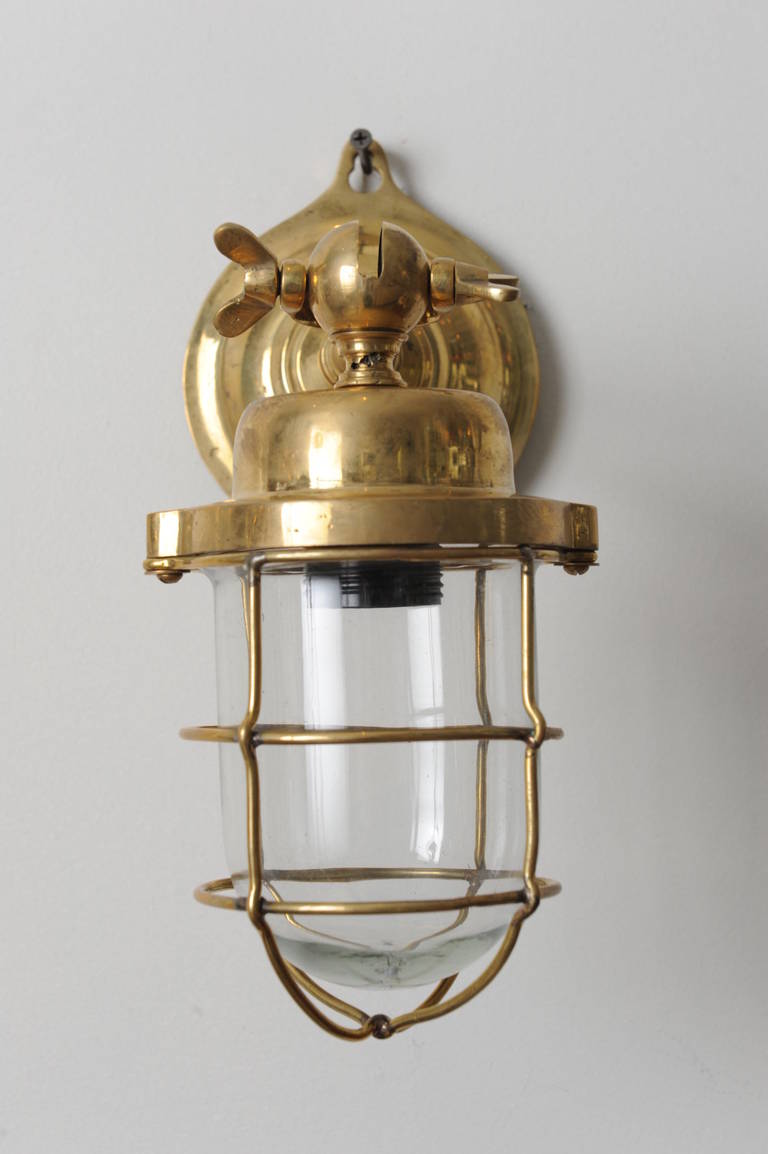 Pair of brass passageway lights from a merchant ship.  The arm is adjustable and could actually hang instead of mount on the wall if so desired.  This is a sealed system with the glass shade and surrounding cage and could be used outside.  Rewired