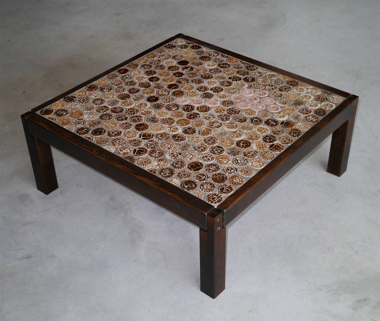 A rare squared low table from the Galaxy range.

The top table consists with numerous round tiles figuring naive faces in various shades from sand rose to warm brown and artistically inlaid in a cement basis.

Wooden frame and feet.

Signed by