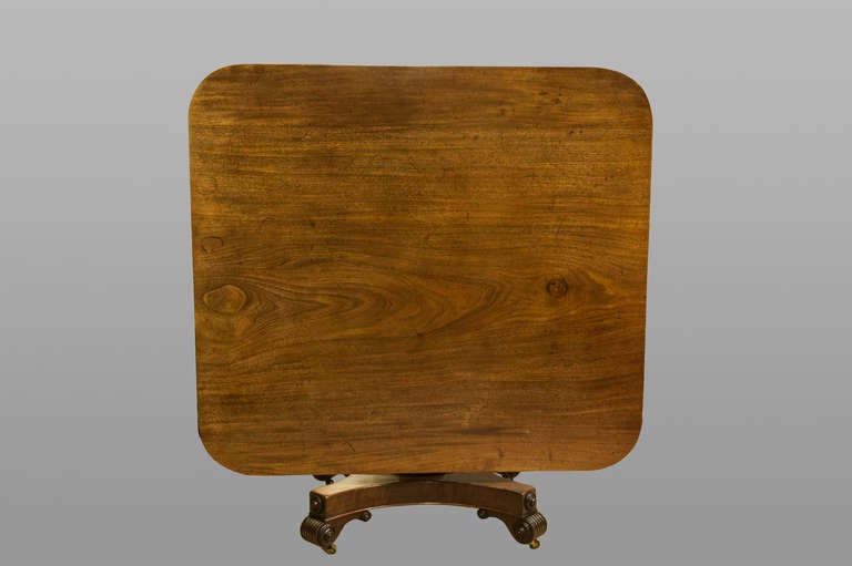 A Handsome Regency Mahogany Tilt Top Centre Table With Its Rectangular Top On A Turned Baluster Stem, Quadrapartite Base And Scroll Feet.