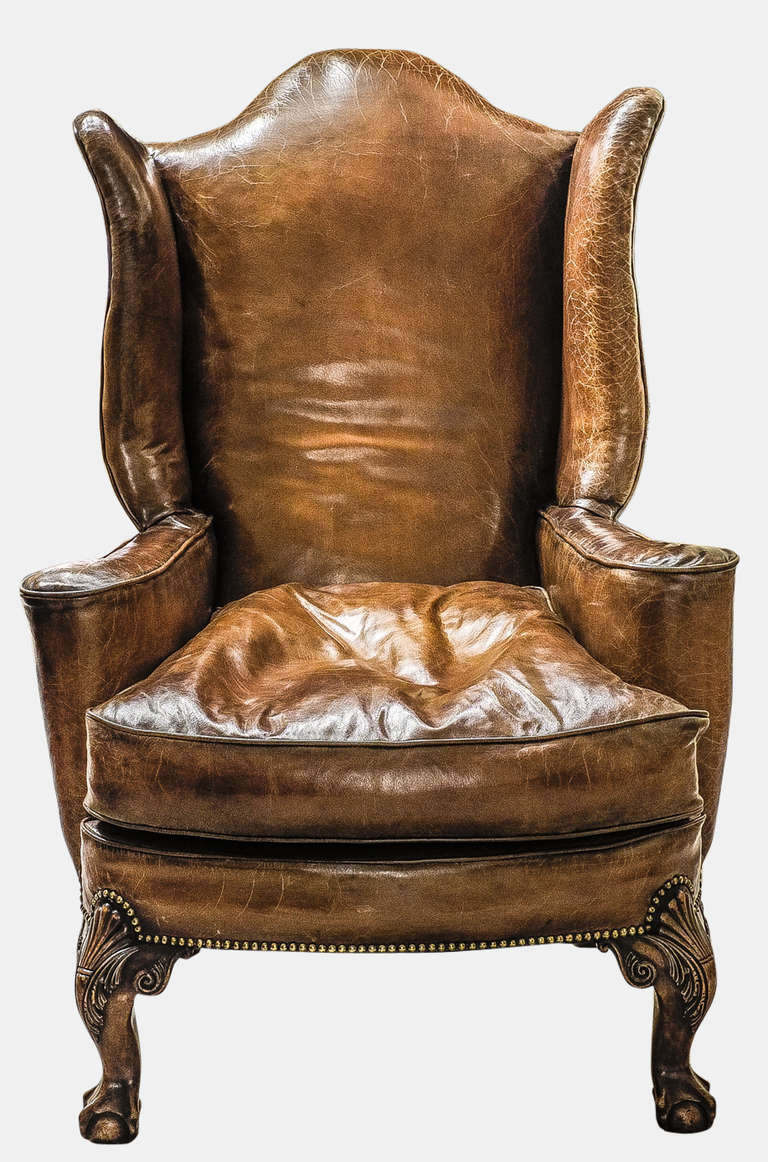 A pair of Queen Anne style wing back armchairs of large proportions, in antique leather hide, and finished with brass stud trim. This is an extremely comfortable pair of luxurious chairs.