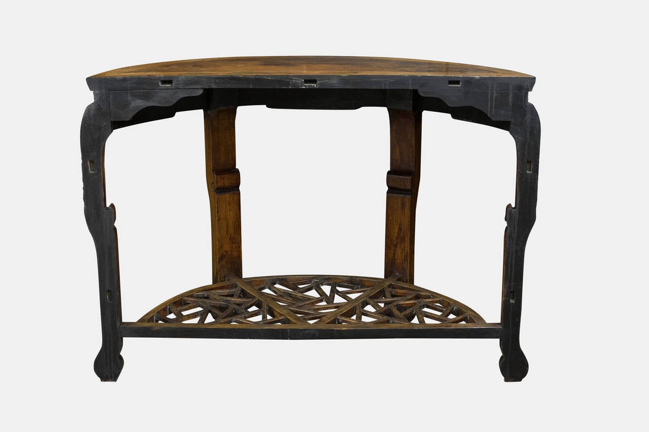 A pair of Chinese Elmwood demilune console tables of large proportions with intricate carved decoration to apron and legs and a lower fretwork shelf. The tables also interlock to create a circular centre table.