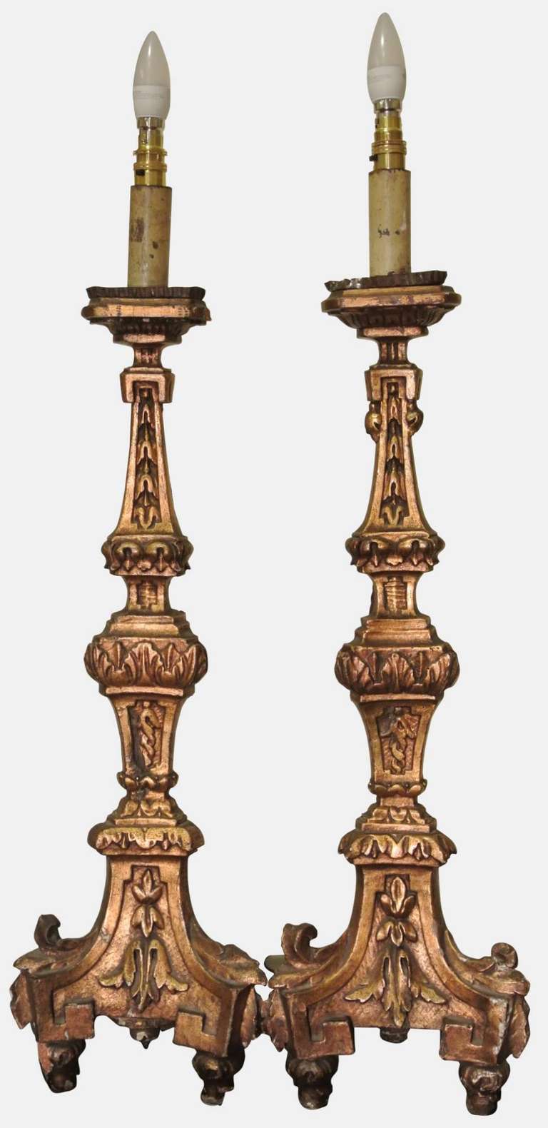 A pair of Italian early 18th century giltwood altarsticks of triform section.
The foliate cast stems descending to spreading triform bases on toupie feet.