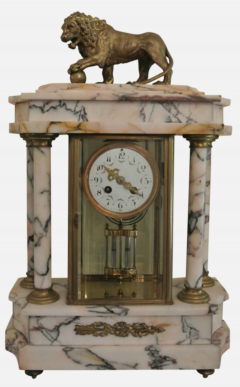 An elegant French white and pink marble clock garniture of neoclassical form, with ormolu decoration, the pediment supported by four columns and surmounted by a bronze lion with his paw on a ball.

Mantel clock dimensions: H 56cm, W 35cm, D 14cm
