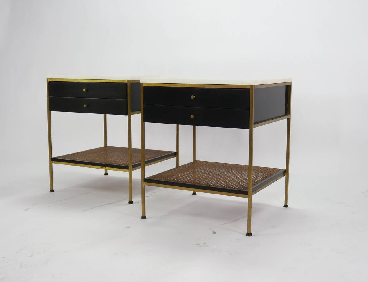 Pair of Paul McCobb for Directional Irwin collection nightstands or end tables. Original vitrolite white glass tops, two drawers, brass frames with caned lower shelves.