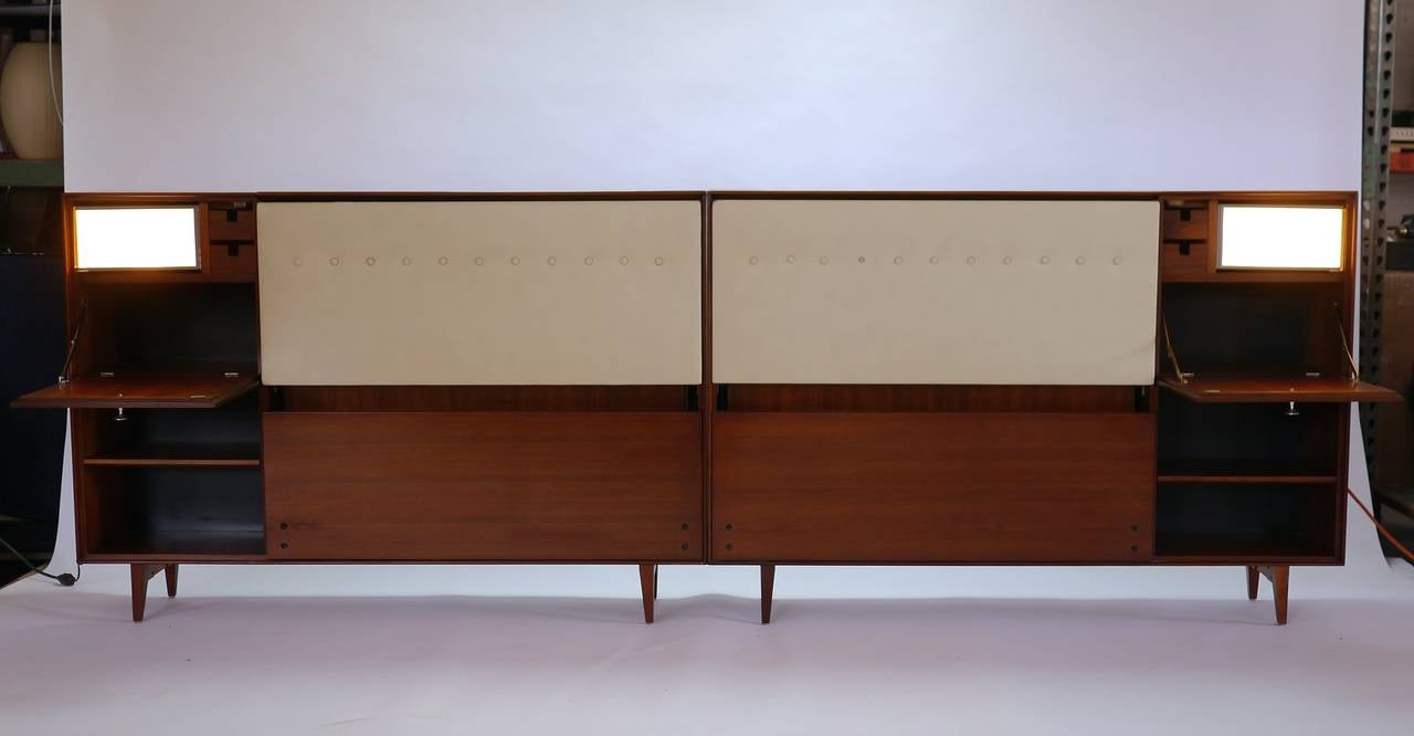 King-size headboard in walnut by George Nelson for Herman Miller. Having two adjustable shelves and two doors concealing storage compartments with two small drawers and lights that swing out. The top can be opened and has more storage space for