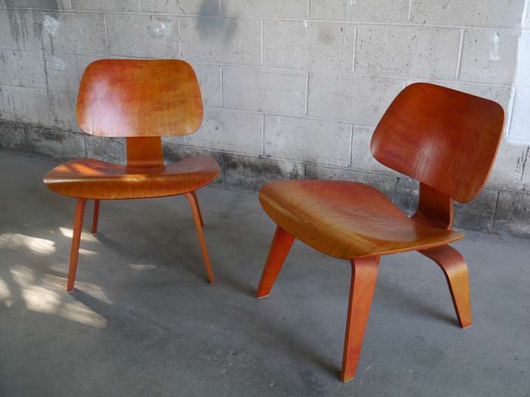 Pair of early red LCW lounge chairs by Charles Eames. Both chairs have aged to a transparent orange / yellow / red patina. The lozenge shock mount and the 5-2-4 screw pattern date these examples to the late 40's or early 50's Each stamped