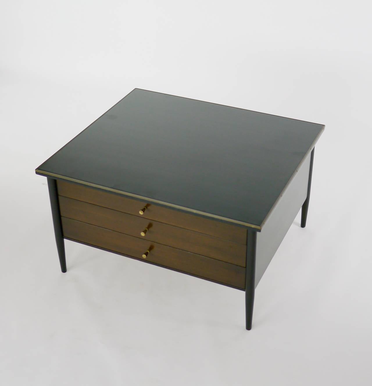 3 drawer side table with chrome pulls. Brass accent to top edges. Black Micarta top. Labeled Connoiseur Collection by Paul McCobb for H. Sacks to drawer interior. Two toned finish, drawers in Walnut, the case in an Ebony finish. 
Designed to