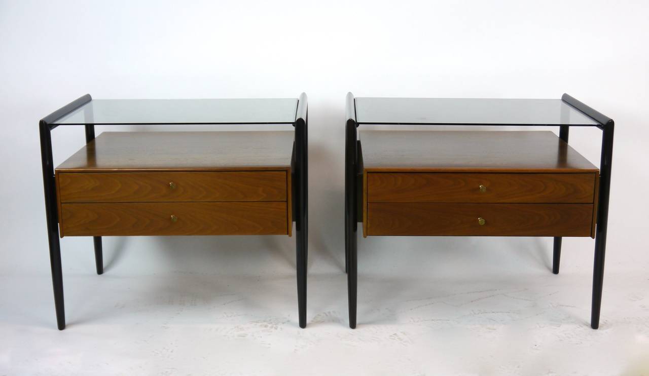 Pair of Drexel Parallel Group nightstands. Walnut and glass topped nightstands from Drexel's Parallel Group having two dovetailed drawers, suspended cabinets and ovoid legs. Machined brass pulls. Done in two-tone lacquer, the legs in dark walnut and