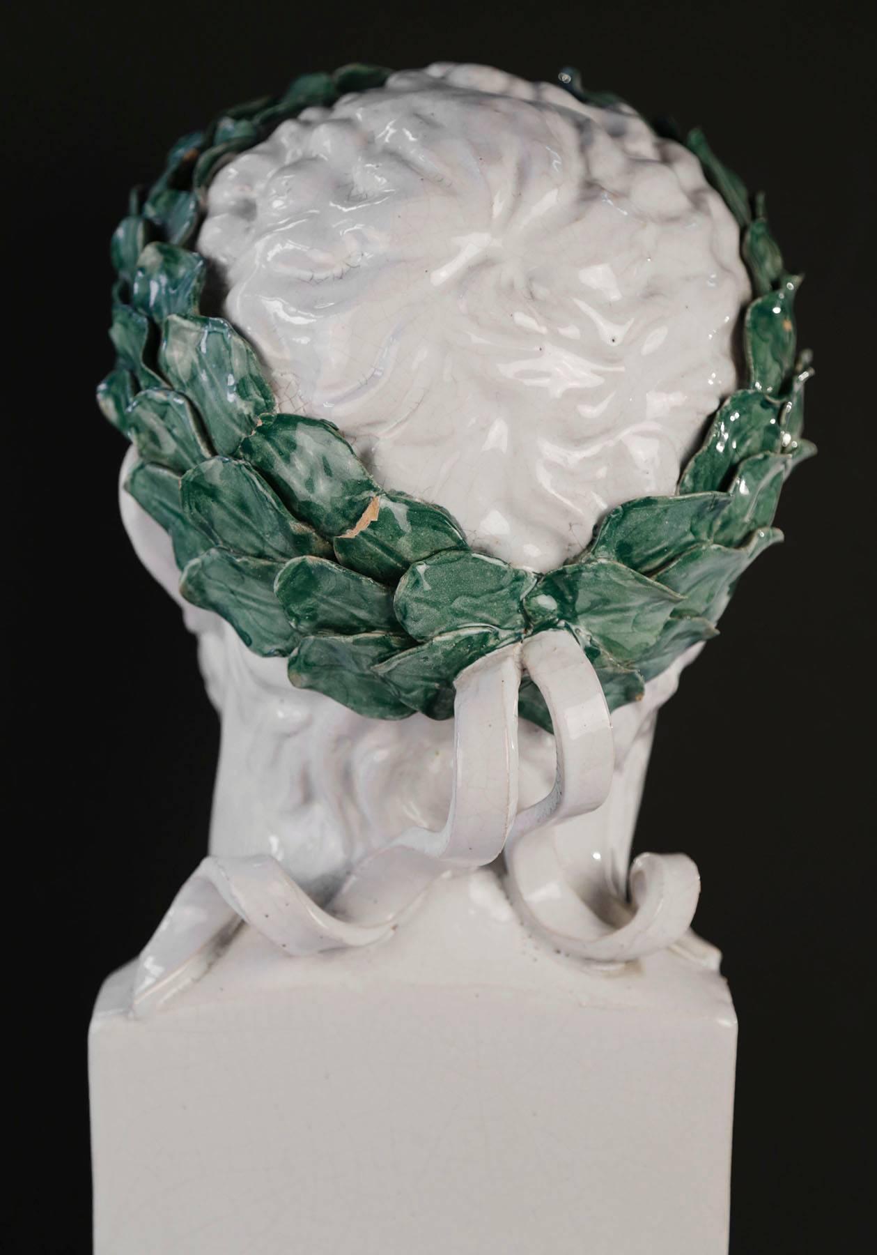 A life sized portrait bust of a Roman emperor, in white slightly crackled glaze, modeled with a green glazed laurel wreath around his head
