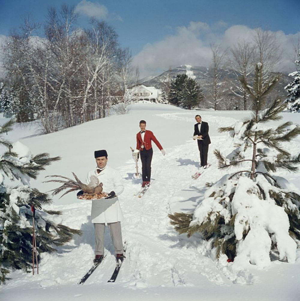 Eaux de ski
Slim Aarons Estate Edition
40 x 40 pouces

Trois serveurs de ski sur une piste de ski, l'homme au premier plan portant un oiseau sur un plateau, le deuxième homme portant un vin dans un seau à glace et le troisième portant un menu, vers