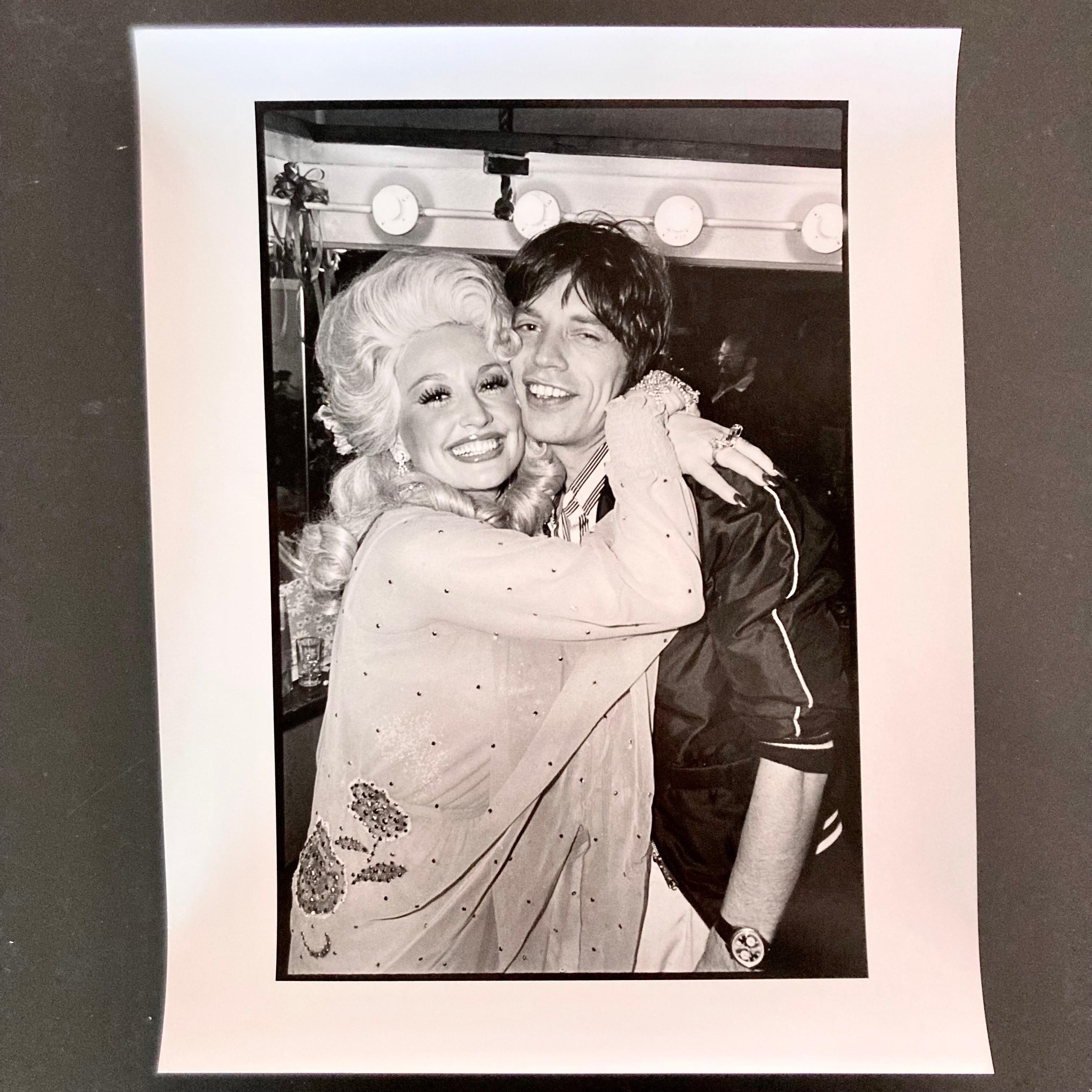 Vintage darkroom print of Dolly Parton hugging Rolling Stones Mick Jagger, taken at The Bottom Line in New York City after a Dolly Parton show in 1977. This print is an original, hand printed darkroom print made by the photographer Allan Tannenbaum.