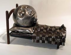Slumber di Rodger Jacobsen è una scultura in acciaio che raffigura un uomo addormentato nel letto.