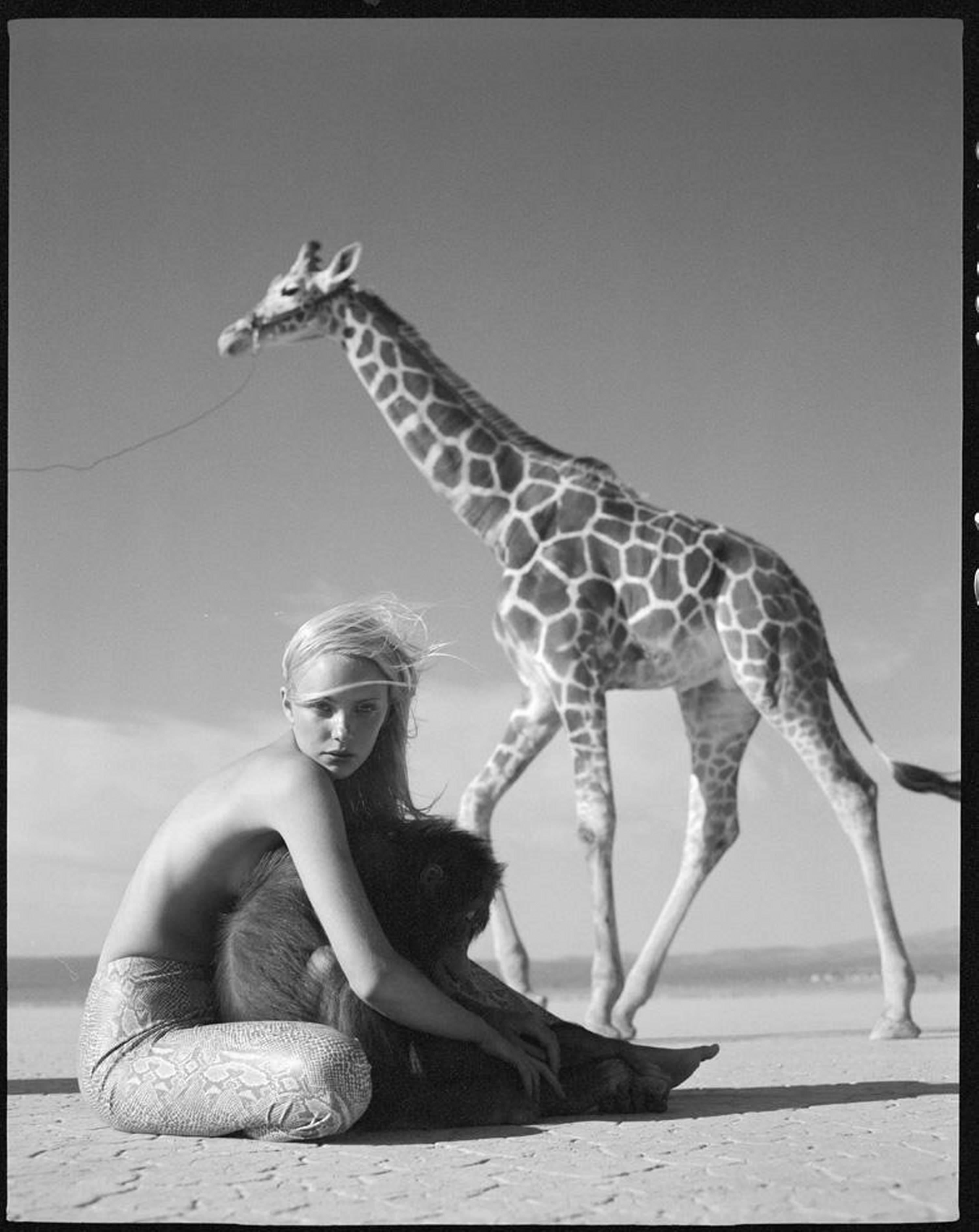 Michel Comte Black and White Photograph - Blond Model sitting shirtless  on the desert hugging a monkey from a giraffe