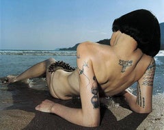 Brazilich-back view of a naked woman with tattoos lying on a beach