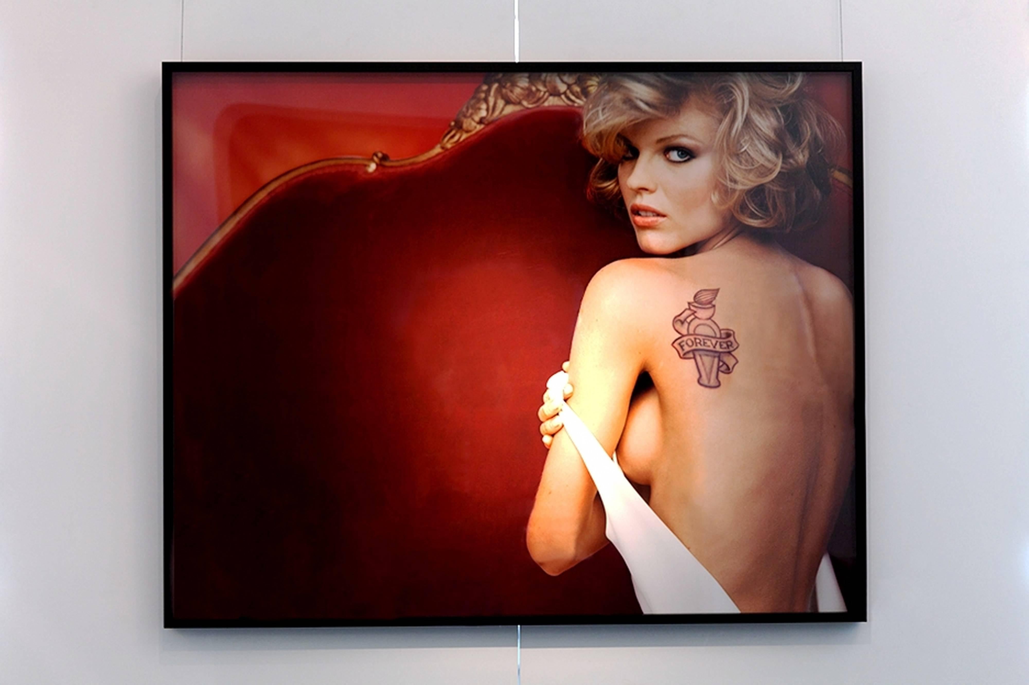 Supermannequin Eva Herzigova sur un canapé rouge montrant son dos nu avec un tatouage  - Photograph de Michel Comte