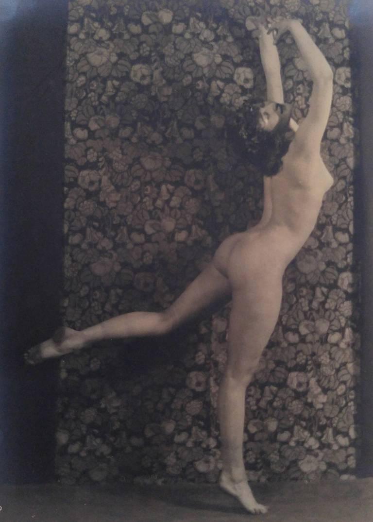 Nude Dancer, de la série The Female Figure de Karl Struss, représente une femme nue debout sur une jambe, la jambe levée dans une position arabesque. Ses bras sont levés au-dessus de sa tête, elle se cambre et tourne la tête vers le spectateur.