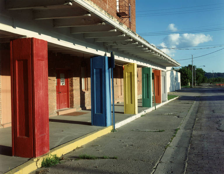 Fort Madison, Iowa by David Graham is a 30 x 40 inch C-Print, available in an edition of 25. This photograph features a building with colorful structures. This photograph is signed, titled, dated and numbered and is mounted to a board. This