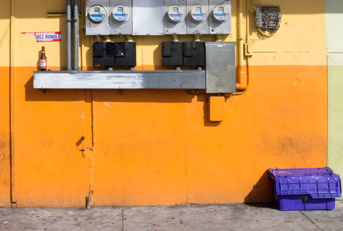 Miami, Florida von David Graham ist ein 16 x 20 Zoll großer Pigmentdruck, der in einer Auflage von 25 Stück erhältlich ist. Dieses Foto zeigt eine orange-gelbe Wand mit elektrischen Geräten und einem lila Kasten. Dieses Foto ist signiert, betitelt,