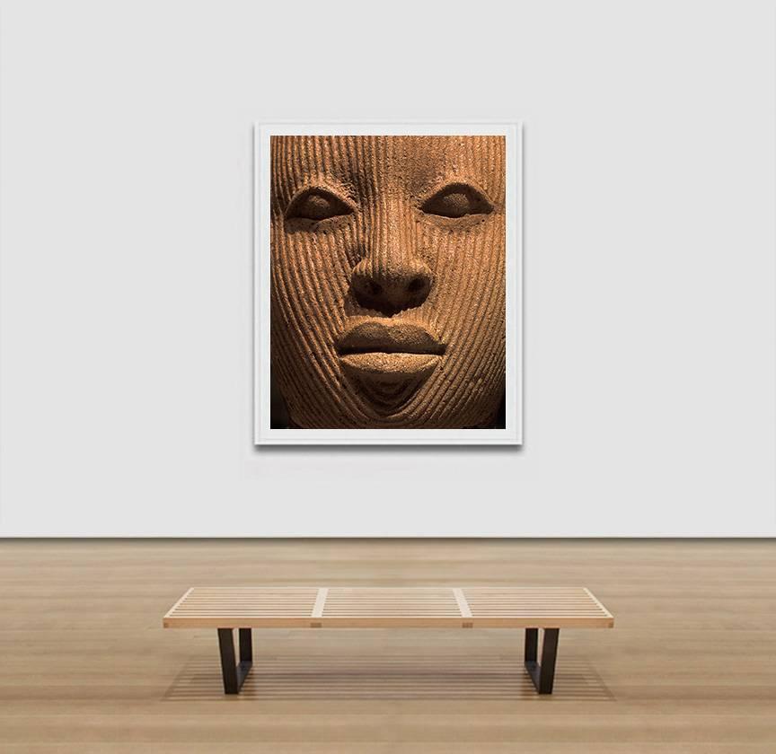 Pierre Sernet's F019, Nigerian, Terracotta is a Large 61 x 50 inches Giclée Print. It is framed. The image is a close-up photograph of a sculpture from a Nigerian Terracotta, only the face can be seen. The artwork is part of the “Face” series, where