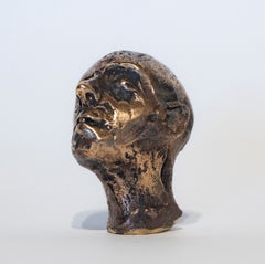 Scultura figurativa in bronzo lucido raffigurante una testa in miniatura con lo sguardo rivolto verso l'alto
