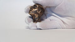 Scultura figurativa in bronzo lucido raffigurante una testa in miniatura con lo sguardo rivolto verso l'alto