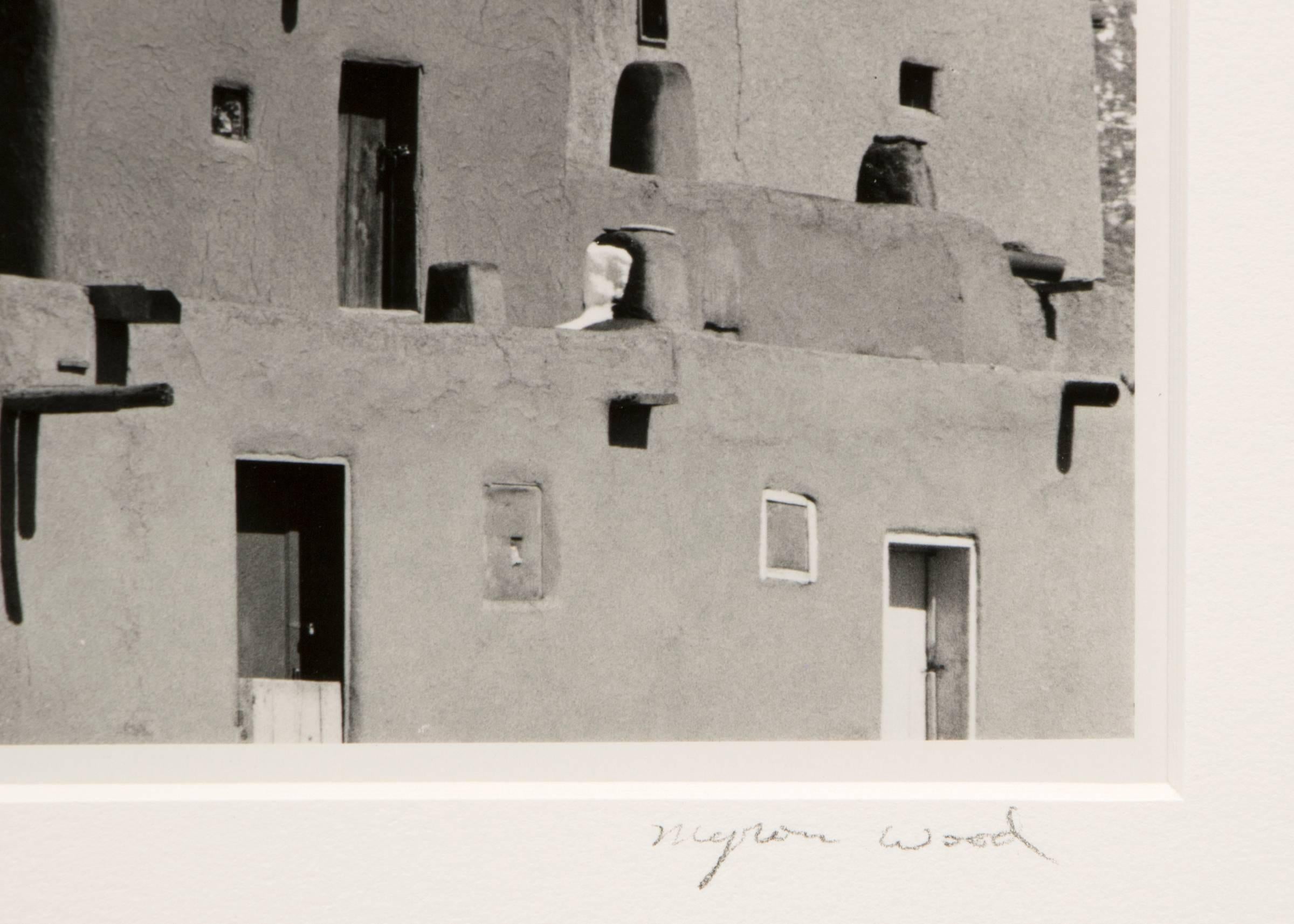 Original signed framed black and white photograph by Myron Wood (1921-1999) of Taos Pueblo, New Mexico in the winter with mountains in the background. Presented in a custom frame, outer dimensions measure 13 ¼ x 16 ½ x ½ inches.  Image size is 6 ¼ x