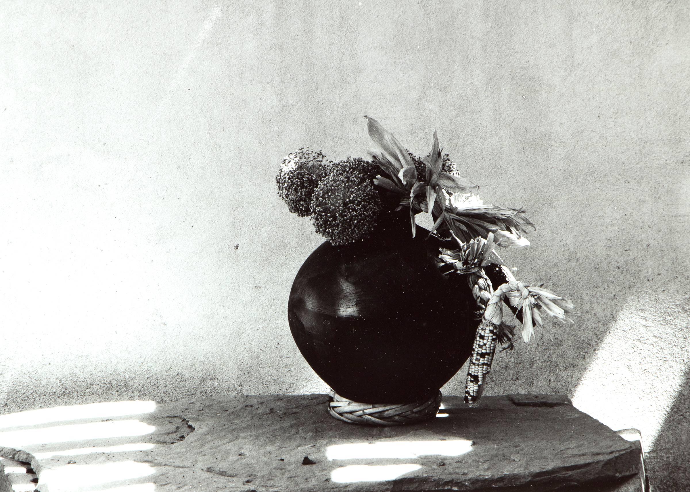 Photographie noir et blanc vintage du Sud-Ouest représentant une nature morte avec une poterie noire Pueblo (amérindienne) avec du maïs séché et un mur en adobe par Myron Wood (1921-1999). Signé en bas à droite et daté de 1980. Présenté dans un