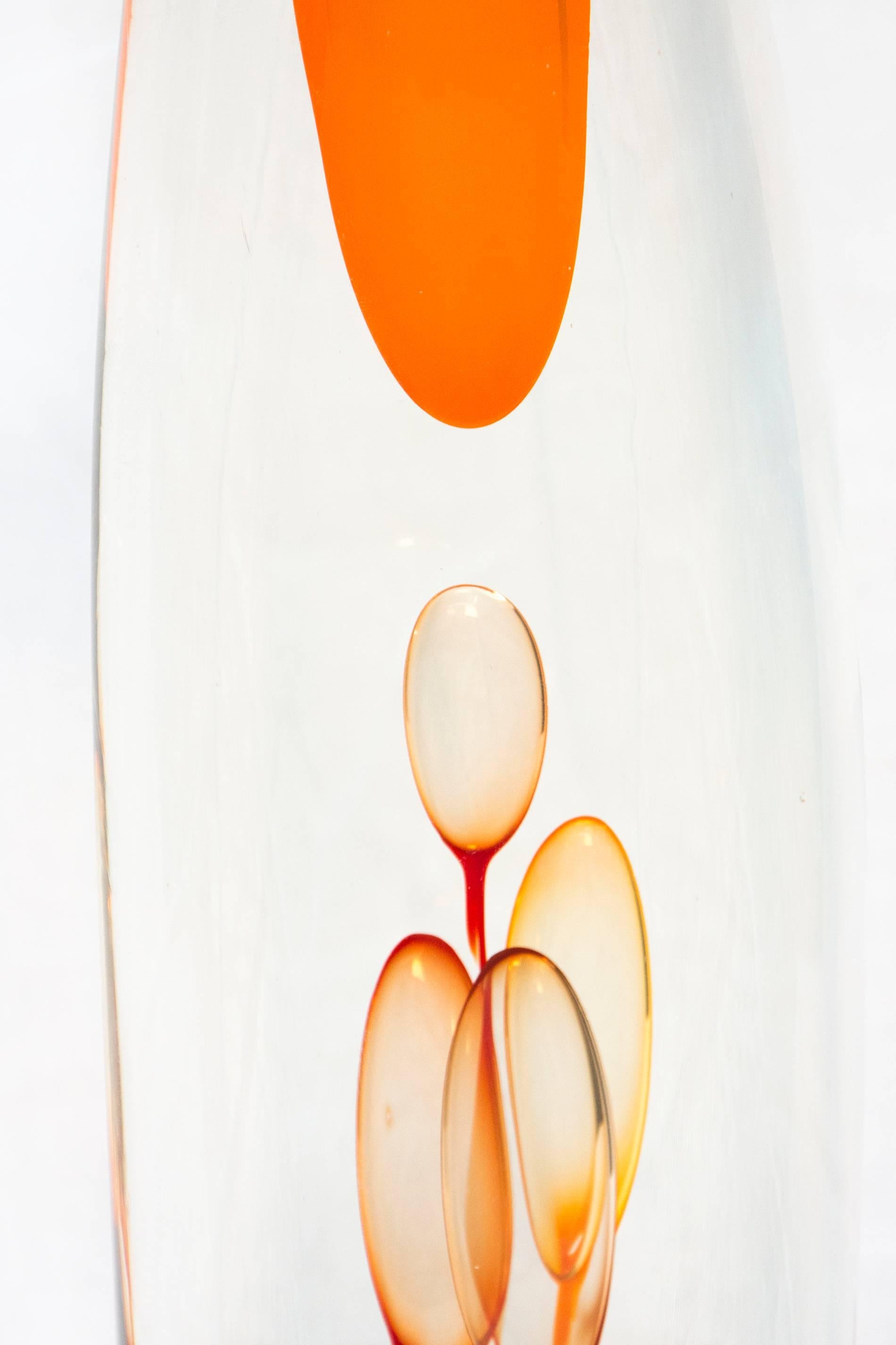 This vibrant and elegant orange blown glass sculpture is created by renowned Australian glass artist, Eileen Gordon. It is tall and thin and its shape is as effortless as a wisp of smoke rising into air. Small bubbles give it the illusion of fluid. 