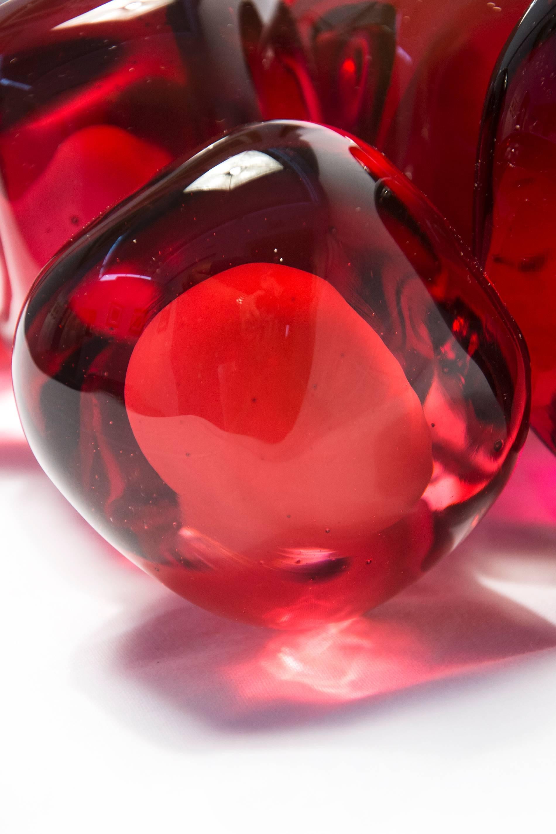 Die länglichen, sinnlichen Formen aus durchscheinendem, rotem Glas haben eine glatte, geschliffene Oberfläche wie die Frucht, die den Granatapfelkern umgibt. Ein einzelnes Samenkorn sitzt neben dem Cluster. Der Granatapfel steht für Reichtum, Glück