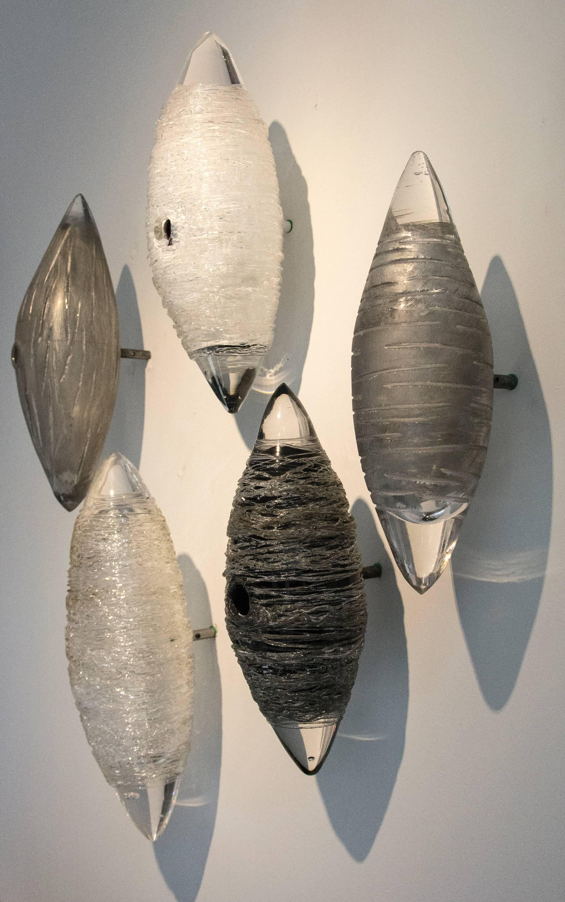 White, clear, silver and black glass wall sculpture.

Reimer’s work references nest-like structures that shimmer as light reflects off the textured and banded surfaces.

 Each element is secured to the wall with a simple pin and bolt mechanism.