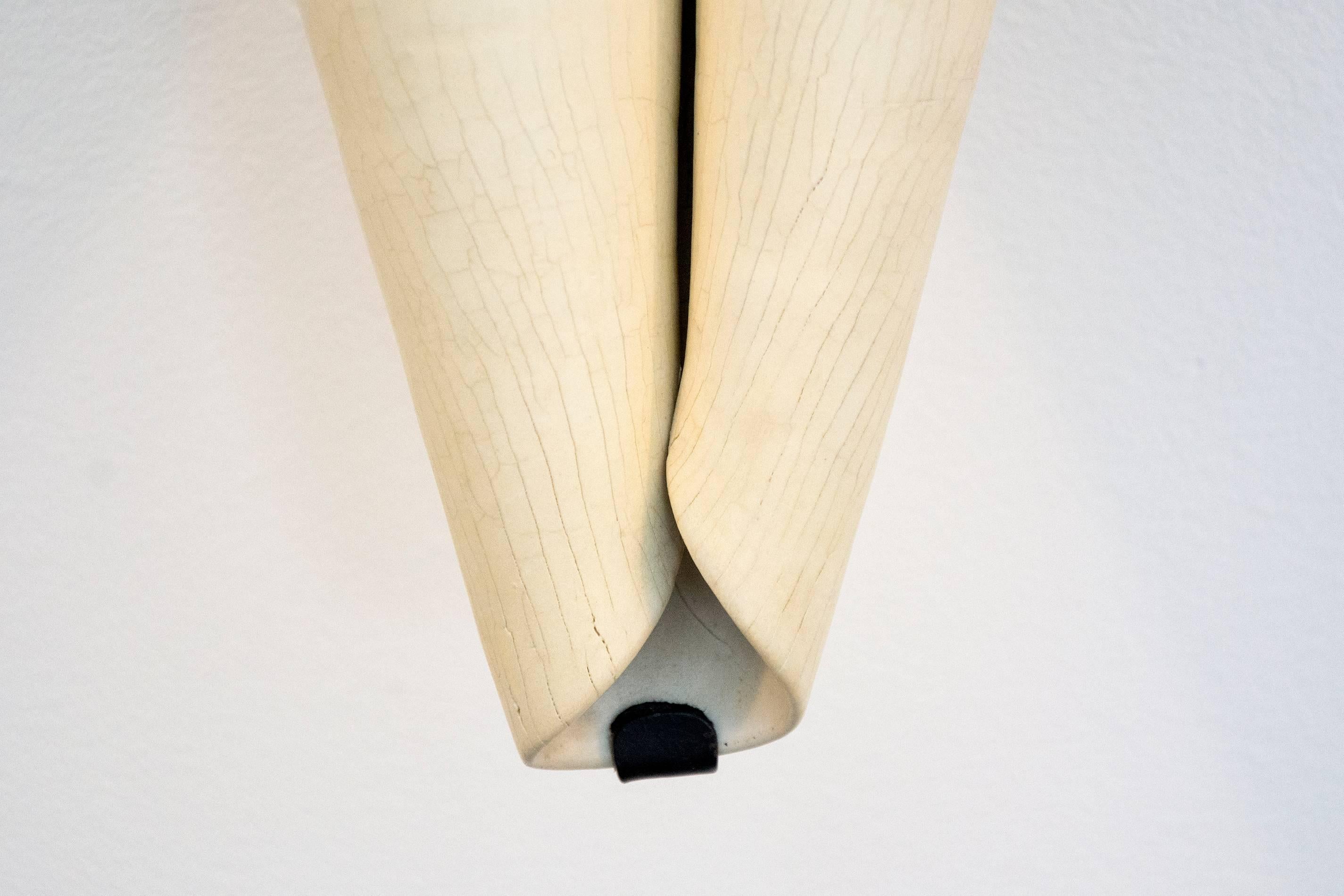 The polished surface of this curled ivory shape is articulated with fissures created through the interaction of fibreglass filaments inserted into the wet porcelain clay before firing. The contemplative sculpture by Paula Murray is wall mounted,