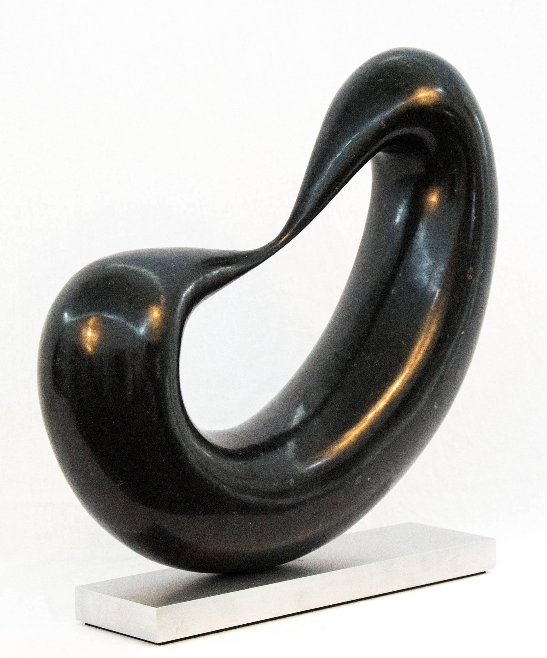 Smooth, black marble flecked with copper and white is engineered into a thick loop that is stretched thin on one side in this table top sculpture. Poised on a flat metal base, the flattened loop features a thinned portion after which the work is