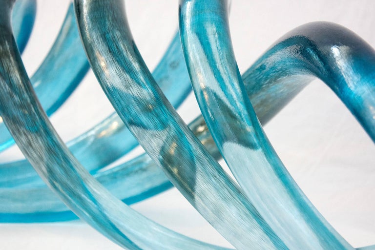 Four lengths of azure blue glass lightly brushed with charcoal intersect in an elegant wave form by artist John Paul Robinson.  

Robinson was educated at the Georgian College of Arts and Technology and the Ontario College of Art, where he later