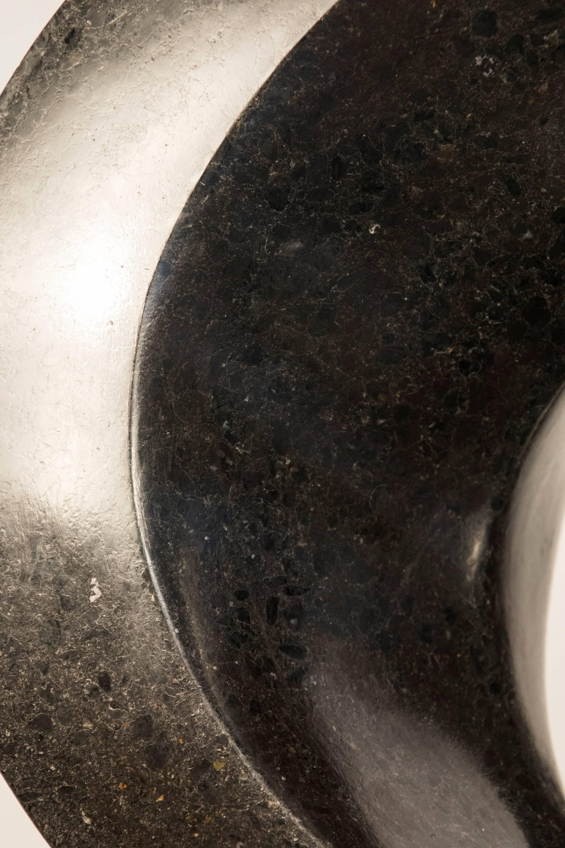 Schwarzer Granit mit glatter Oberfläche:: fast unmerklich mit Kupfer und Weiß gesprenkelt:: wurde zu einem eleganten Band verarbeitet:: das einen spürbaren Kontrast zu seinem Gewicht bildet.  Diese Arbeit hat eine Stahlunterkonstruktion und sitzt