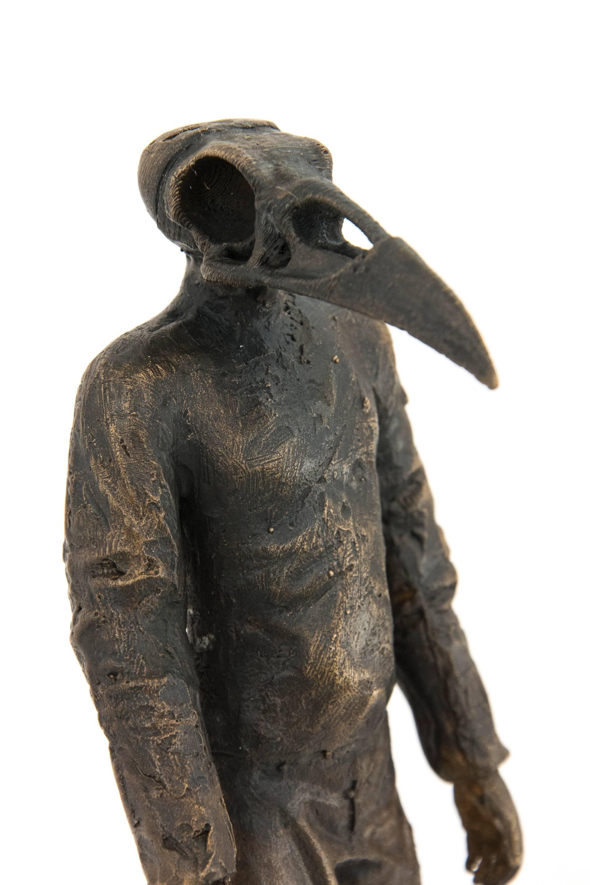 A fully clothed action figure with a raven's skull as a head is cast in bronze. The enigmatic figure teeters on its heels, perched like a bird on a short bronze branch. In this work, the artist draws on the themes of darkness and mystery often