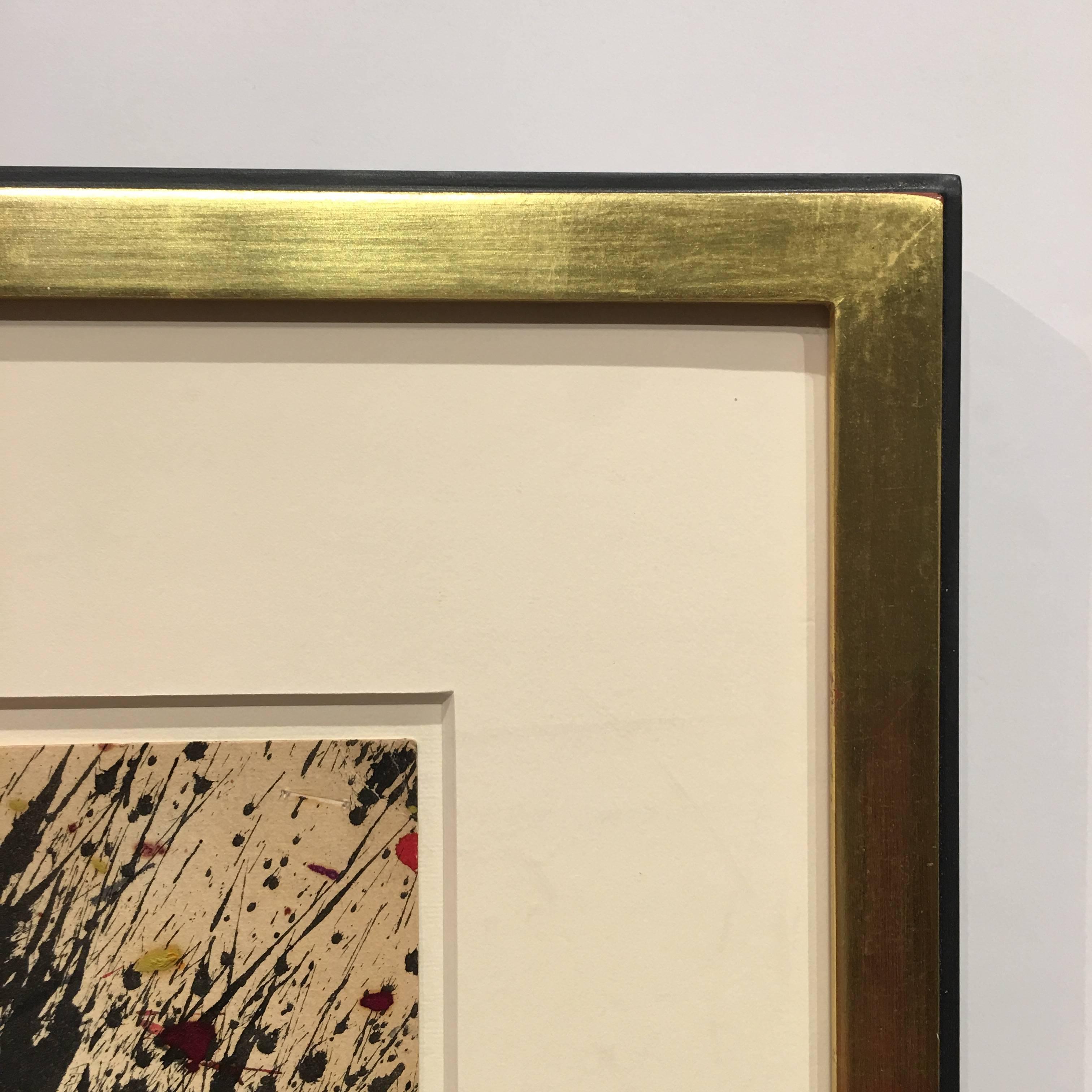A colourful abstract painting composition using watercolour and oil in black, blue, red and warm yellow shades, applied as drips, splatters and streaks that energetically cover the cream paper.

This work is presented in a gold frame with black
