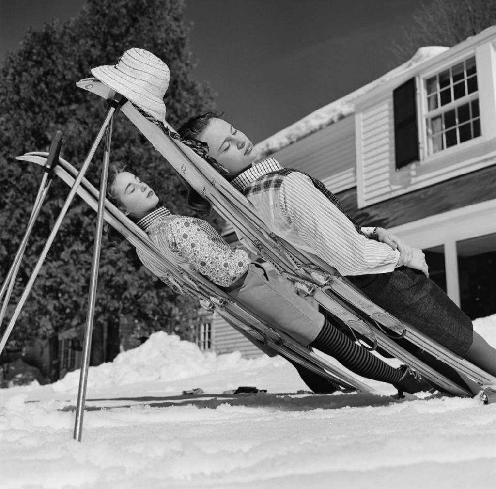 'New England Skiing' by Slim Aarons

Two women recline on improvised sunbeds in New Hampshire, 1955.

Two fashionably dressed young women, take a break from the ski slopes and have a siesta on their skis, behind them you can see a typical clapboard
