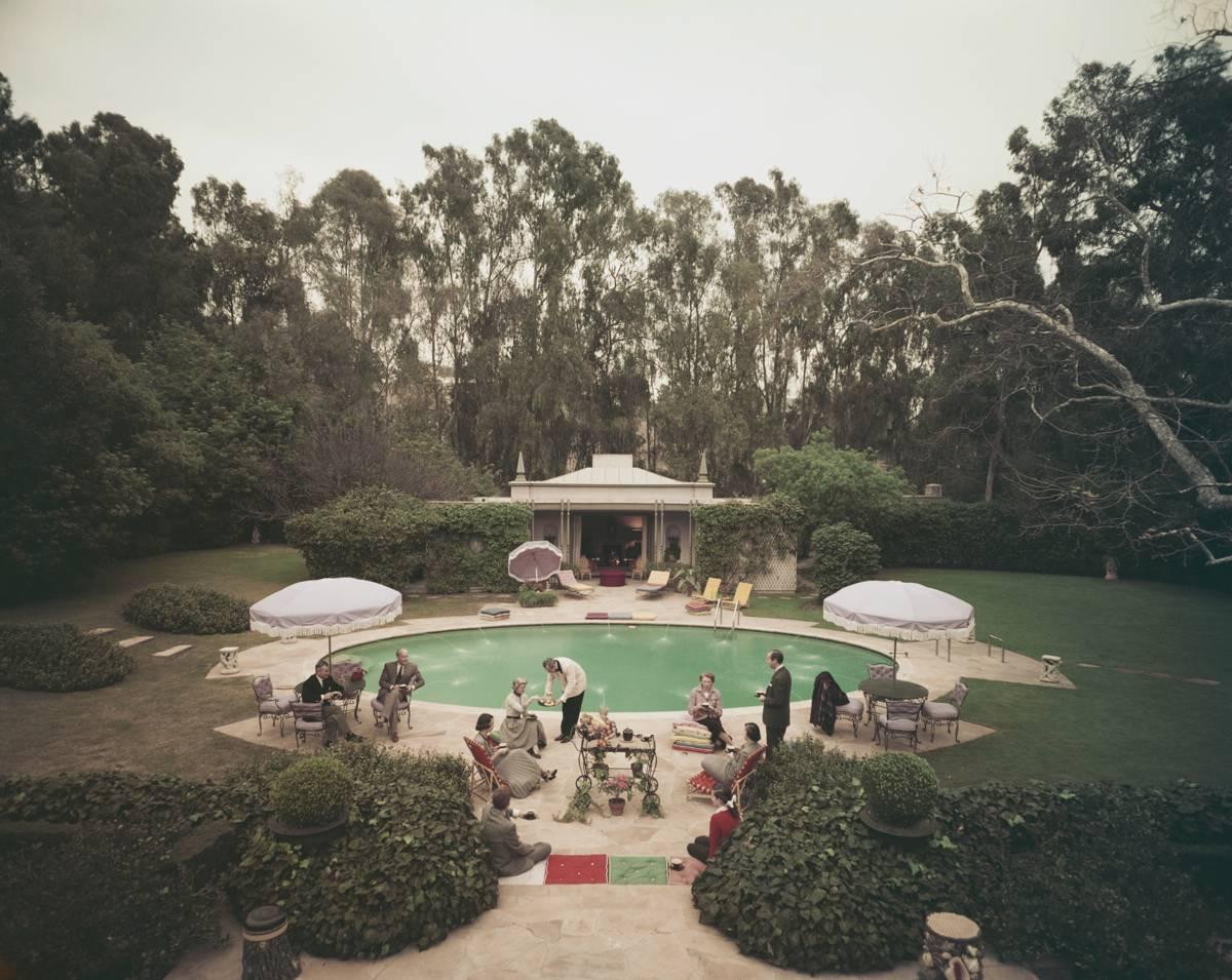 'Scone Madam' by Slim Aarons

Afternoon tea round the pool on a cold day at the home of interior decorator James Pendleton in Beverly Hill, 1960. 

Fashionably smartly dressed guests enjoy afternoon tea  served by a butler beside the swimming pool