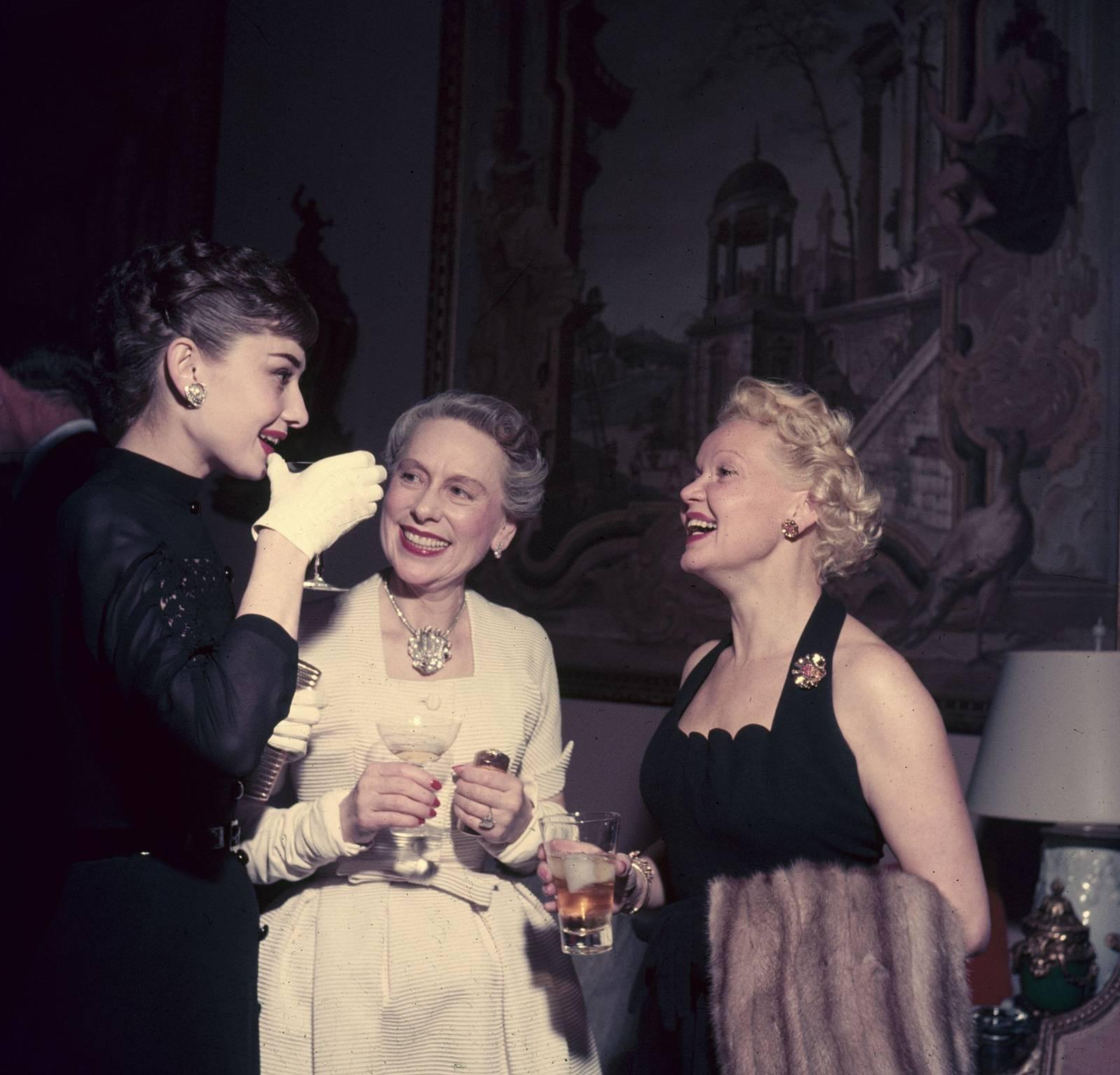 On the left film star Audrey Hepburn (1929 - 1993) talks with Mrs Grover Magnin (centre) and another guest at a party in San Francisco, 1953.

The beautiful and fashionable movie star and style icon dressed in her eponymous look; all in black with