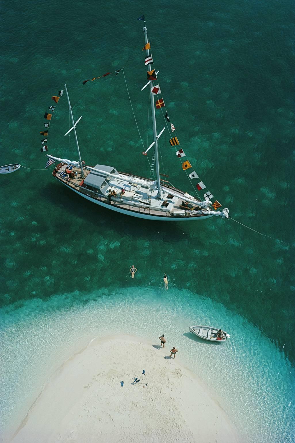 A yachting holiday on Exuma in the Bahamas, April 1964.

A stunning large yacht, festooned with colourful world flags is anchored close to a gorgeous white sand island, where two figures are standing looking out across the vivid turquoise then green