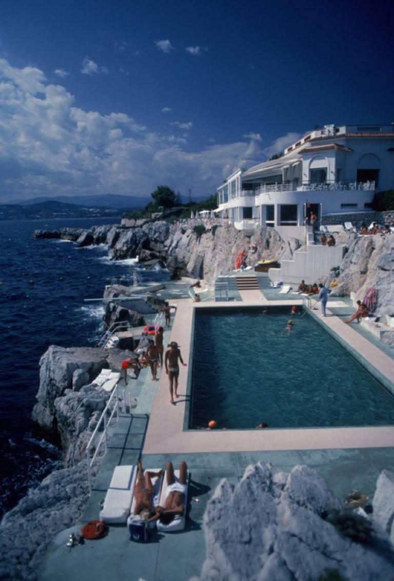 Hôtel Du CAP Eden-Roc" de Slim Aarons

Des clients se détendent au bord de la piscine de l'hôtel du Cap Eden-Roc, Antibes, France, août 1976.

Une scène tout simplement magnifique. Les clients à la mode et élégants se détendent dans et autour de la