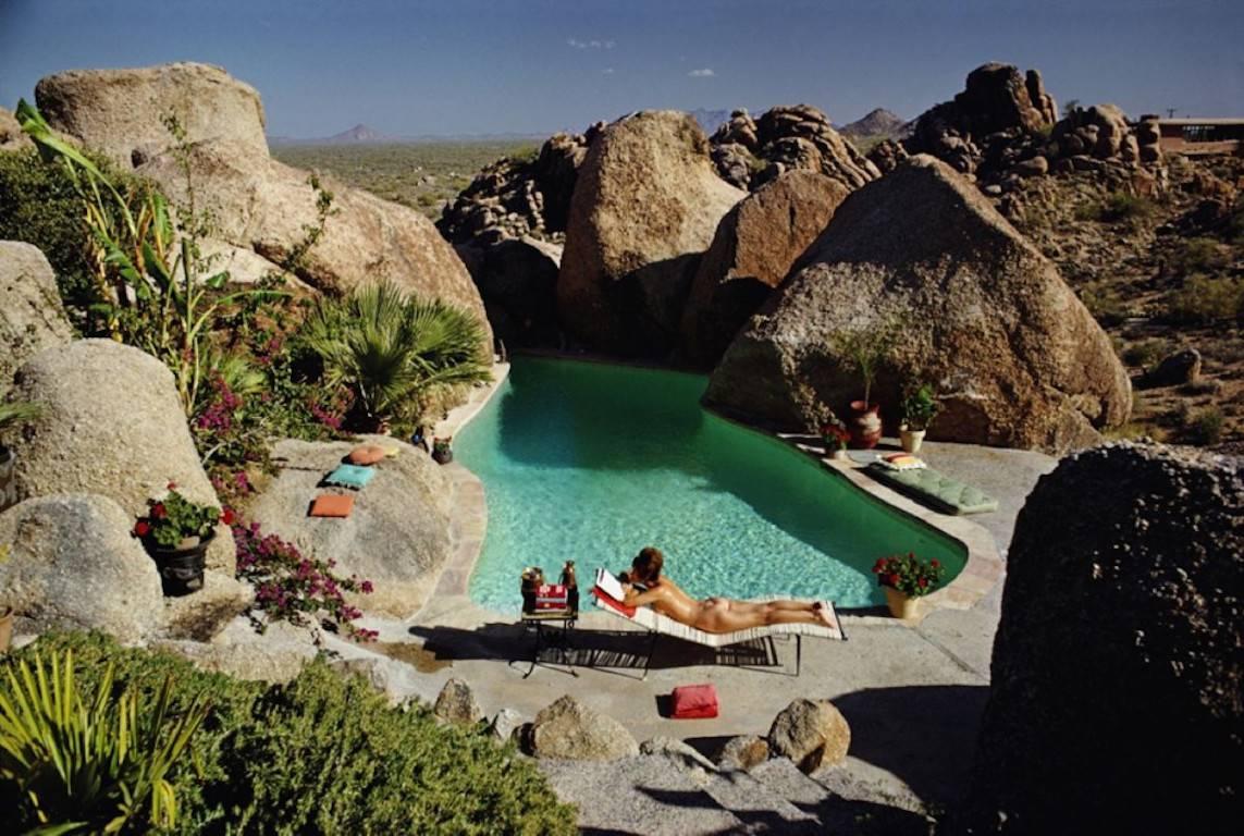 'Sunbathing In Arizona' by Slim Aarons

A woman sunbathing nude by Tom Darlington’s pool in Carefree, Arizona, April 1967. 

A gorgeous swimming pool with crystal clear turquoise waters is nestled in amongst some giant boulder rocks where a young