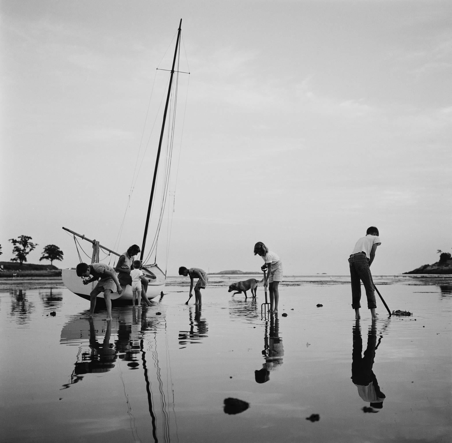 'Digging For Clams' by Slim Aarons

Mrs. Leverett Saltonstall Shaw watches her children digging for clams at low tide on Black Beach, with a sail boat on the sand behind them and joined by their dog in Massachusetts Bay, circa 1960. 

The image has