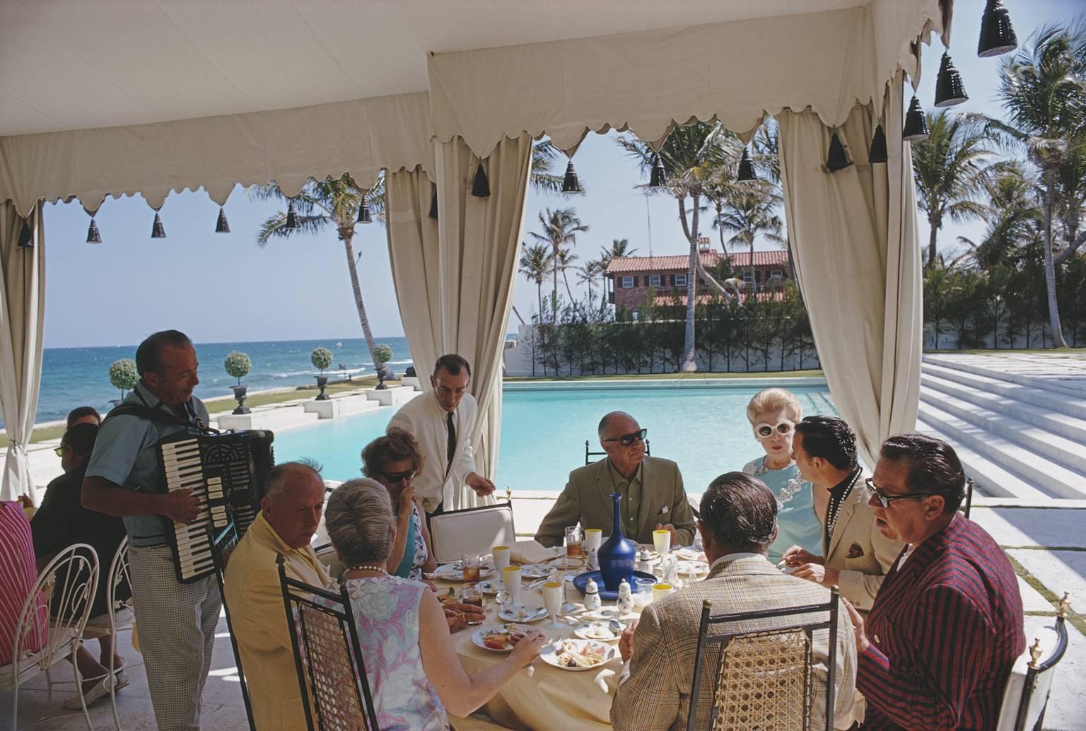 'Dining at Wilmot's' by Slim Aarons

Accordion music accompanies a meal by the pool at the home of Molly Wilmot in Palm Beach, Florida, April 1968.

This photograph epitomises the travel style and glamour of the period's wealthy and famous,