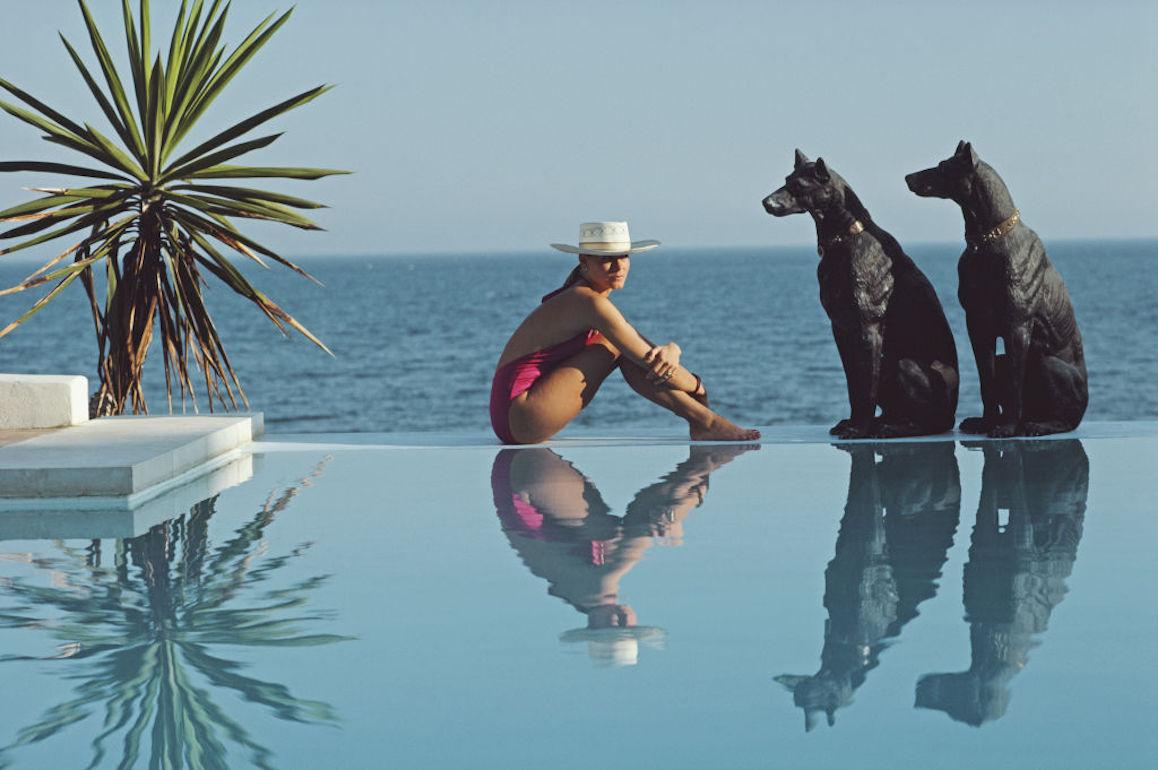 Laura Hawk, Assistentin des Fotografen, entspannt sich am Pool von El Rincon, dem Haus der von Pantz in Marbella, Marbella, Spanien, 1985. 

Dieses Foto verkörpert den Reisestil und den Glamour der Reichen und Berühmten dieser Zeit, der von Aarons