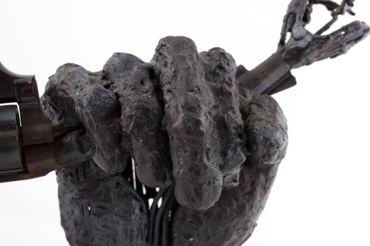In this welded steel sculpture in bronze by sculptor John Kearney, the artist sculpts a textural, clenching fist holding a fire arm. The fire arm is bent by the strength from this clenching fist. Signed and dated on the marble base.

Kearney was